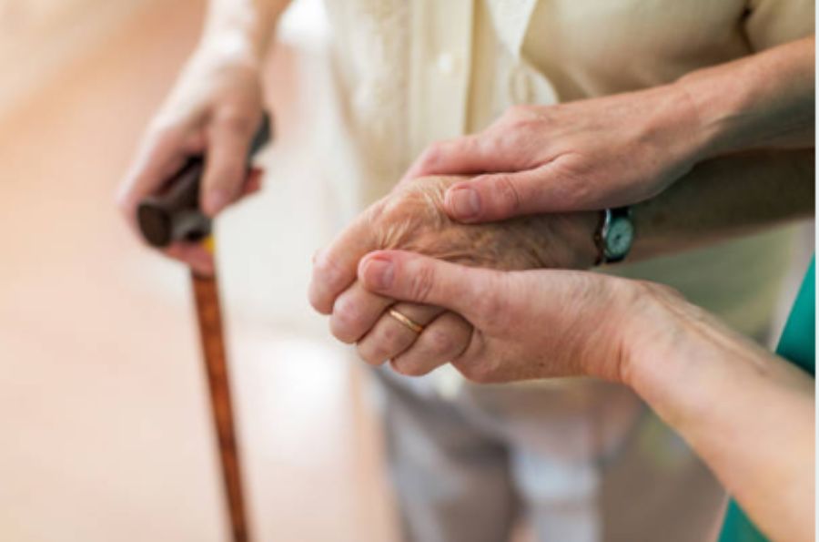 Manos en primer plano que cogen una mano de una persona con bastón
